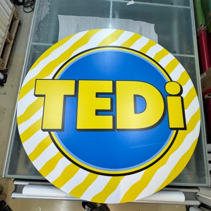Von der Rechinger Werbetechnik GmbH produziertes rundes TEDi-Logo-Schild mit gelb-weißem Rand für den Einsatz auf einem Messestand.